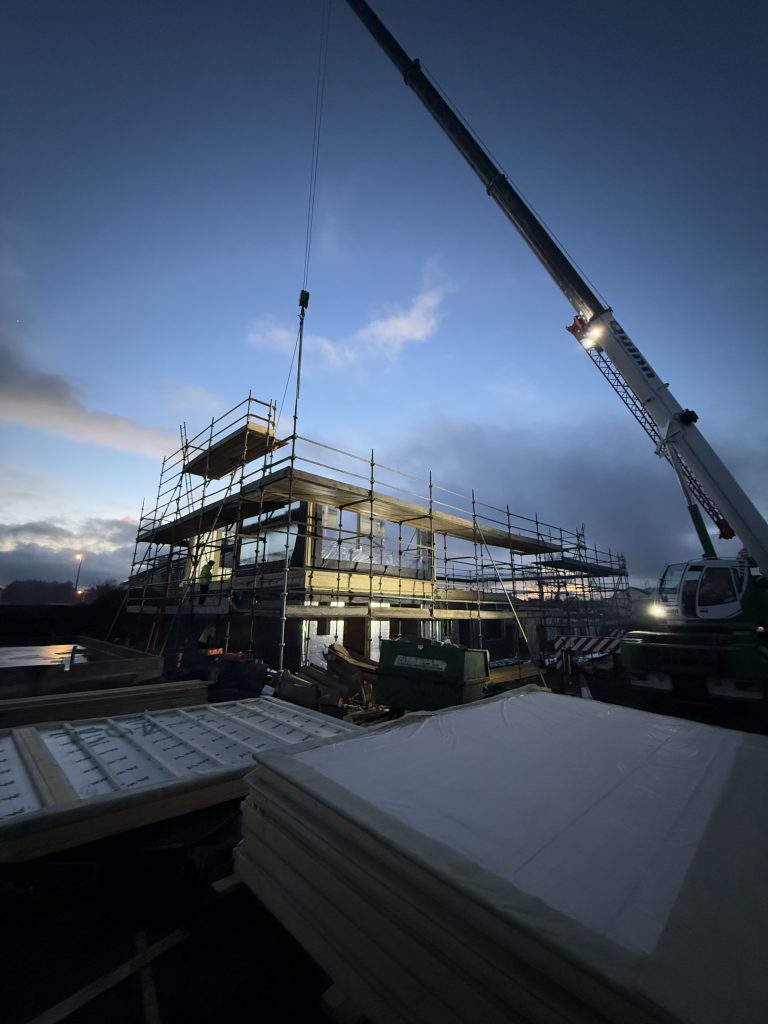 Crane lifting timber frame elements at dusk on a WE Element development site